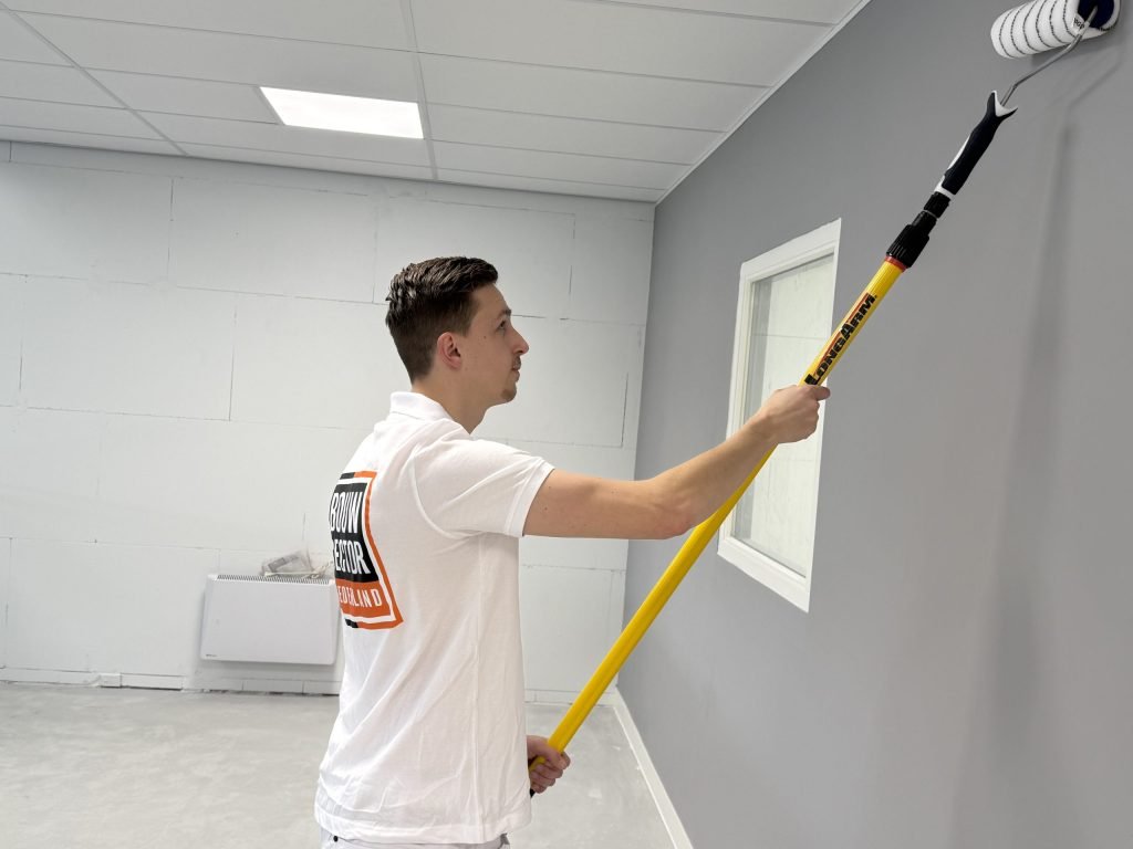 Schilder rolt een grijze wand met een lange verlengsteel in een ruimte met systeemplafond