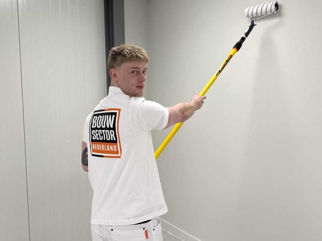 Schilder kijkt over zijn schouder terwijl hij de bovenkant van een lichte wand rolt
