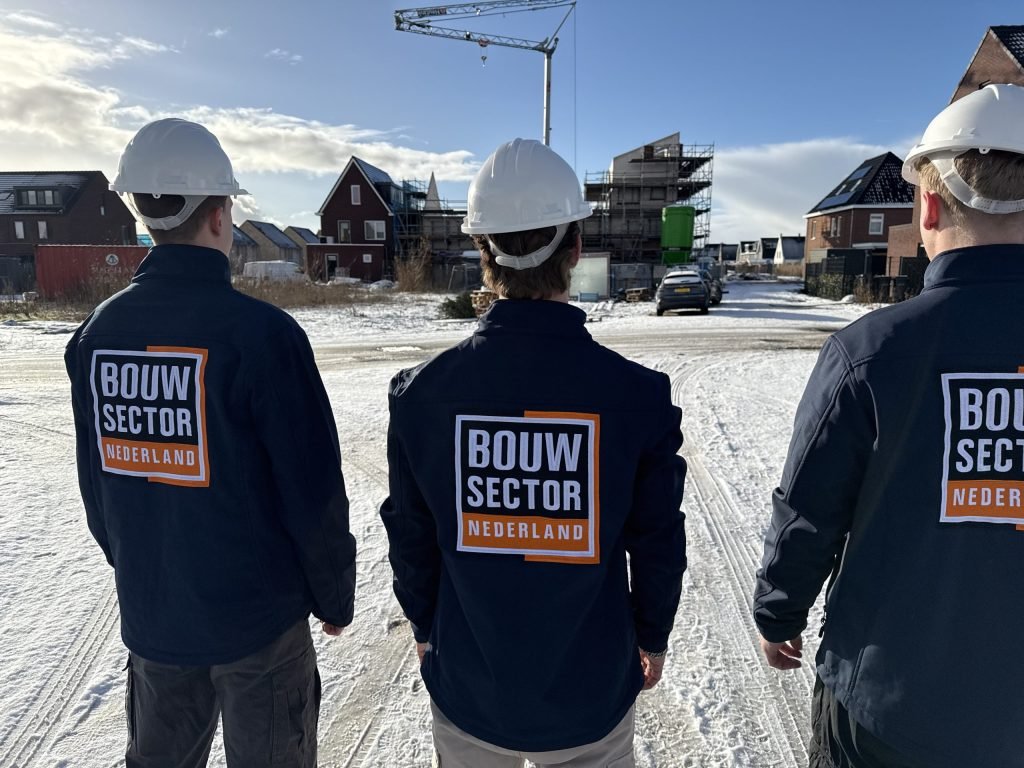 Drie vakmensen van Bouwsector Nederland met witte helm op een besneeuwde bouwplaats met nieuwbouwwoningen